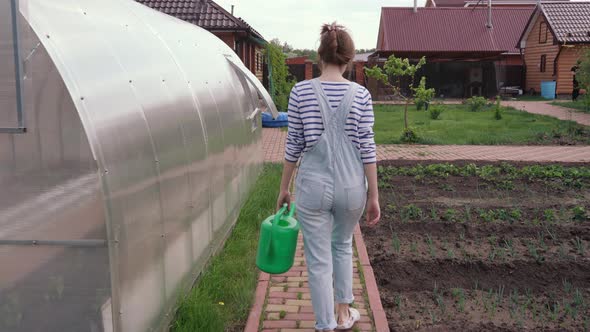 A Farmer Girl Walks with a Green Watering Can Through Her Garden