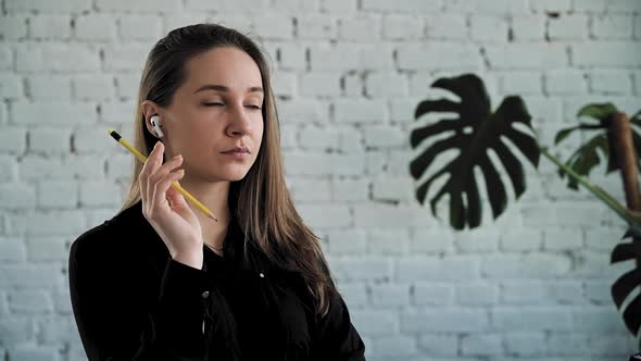 Corporate Woman Thinks and Holds a Pencil in Hands on Headphones Looking to Sides