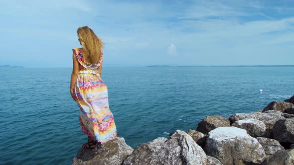 Girl in a Beautiful Dress on Stones Looking at the Ocean