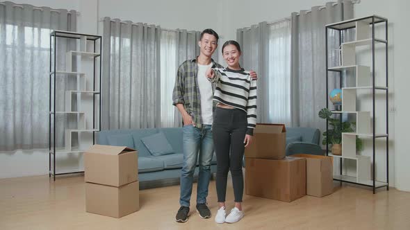 Young Asian Couple With Cardboard Boxes On The Floor Smiling And Showing The Keys To Camera