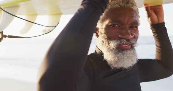 Portrait of happy senior african american man carrying surfboard on sunny beach