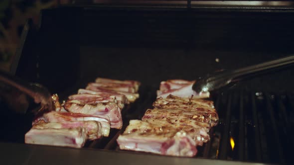 Two sets of Tongs flipping Glazed Lamb ribs across a gas barbeque