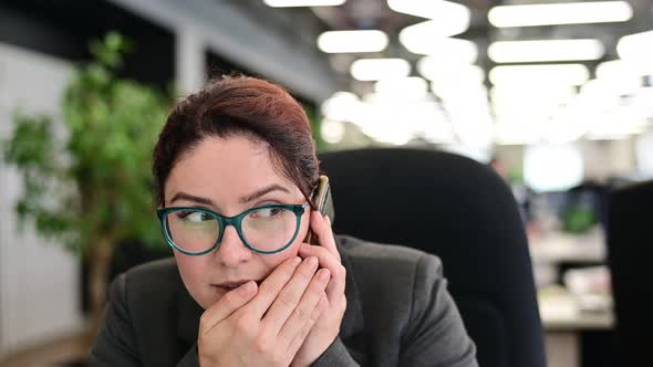 A Woman Sits in an Office at Her Desk and Gossips on the Phone