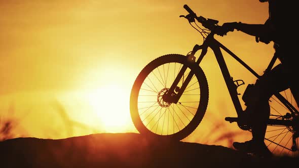 Sportsman biker walk with bike outdoors at golden sunset. Silhouette of a bicycle and a cyclist