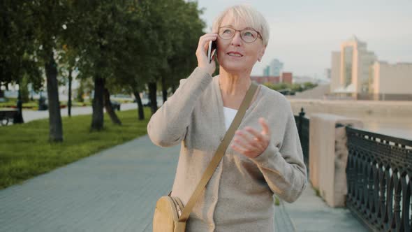 Slow Motion of Joyful Elderly Woman Talking on Mobile Phone and Smiling Walking in City Alone