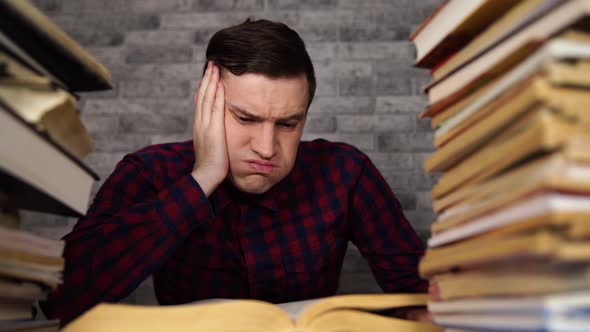 Man Student Boring Reading Book at Library with a Lot of Books in University. Student Disheartened