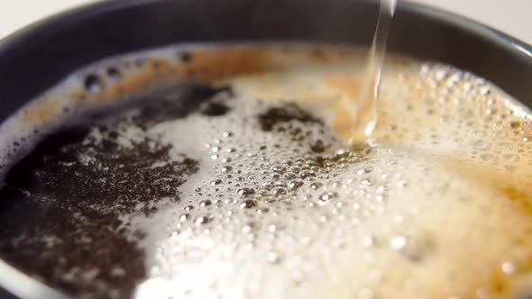 Pouring black espresso coffee into a cup in slow motion with foam and bubbles. Macro
