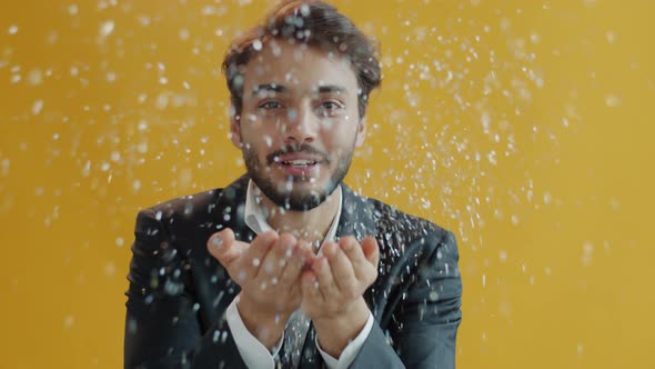 Portrait of Carefree Arab Guy Blowing Silver Confetti at Camera and Dancing