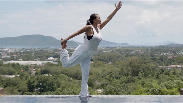 Barefooted Woman in Standing Bow Pose Near Swimming Pool Against Green Forested Islands