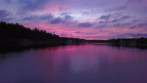 Aerial backward drone shot close to the water, above a lake and towards the forest, a purple sky, at