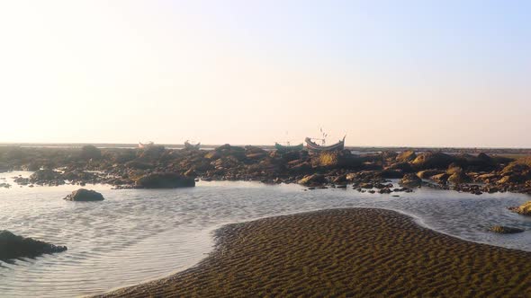 Tide pools at low tide on a rocky shoreline with fishing boats in the background