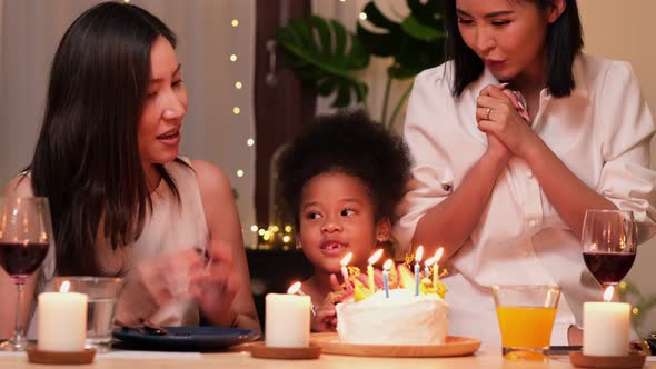 Happy little girl celebrating her birthday with Lgbt family blowing out the candles