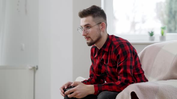 Side View of Exhausted Male Gamer Using Game Controller Sitting on Armchair at Home