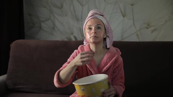 Woman Watching a Late Night Movie at TV, Eating Popcorn. Bathrobe, Facial Mask