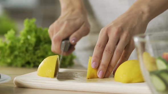 Woman cutting lemon and squeezing juice to glass bowl, vegetable salad dressing