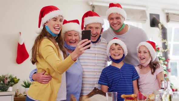 Caucasian family wearing santa hats and face masks around their necks taking a selfie together using