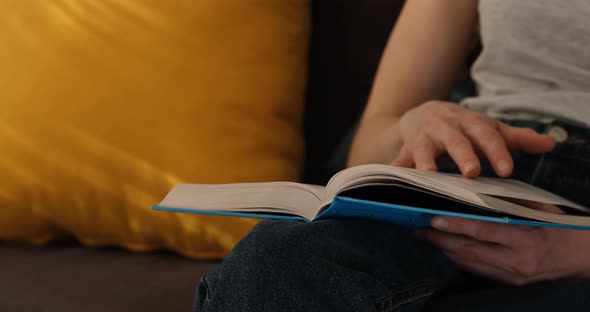 Young woman reading book and turning page. Girl holds paper book in her hands. Close up.
