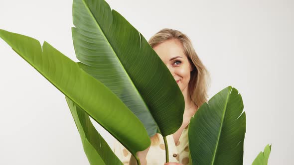 Attractive Caucasian Blueeyed Blonde Girl Behind the Green Leaves Smiling and Looking Into the