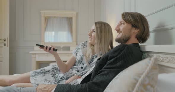 Happy Young Couple Is Lying on Bed and Watching TV at Home