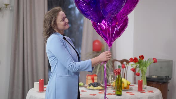 Side View Portrait of Happy Excited Adult Woman Releasing Balloons Indoors at Home on Valentine's