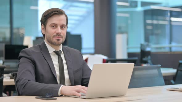 Businessman Smiling at Camera While Using Laptop in Office