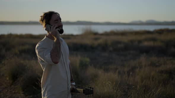 Close Up Portrait of a Cool Guy Calling with a Cellphone and Nodding Holding an Acoustic Guitar in a