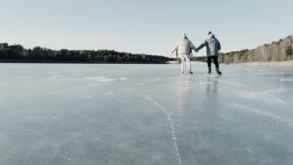 Aerial Shot of Couple Skating on a Blue Frozen Lake in Beautiful Sunny Landscape