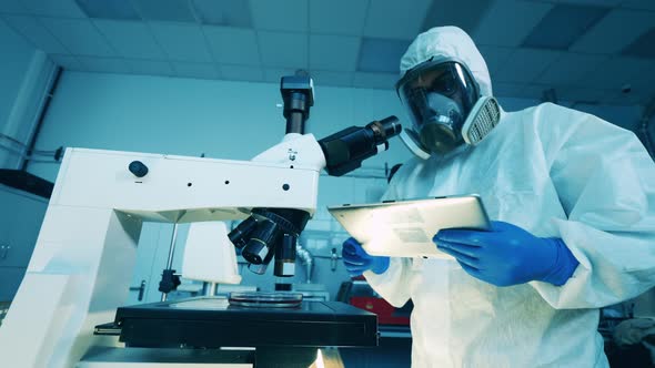 Scientist in a Hazmat Suit is Operating a Microscope in the Laboratory