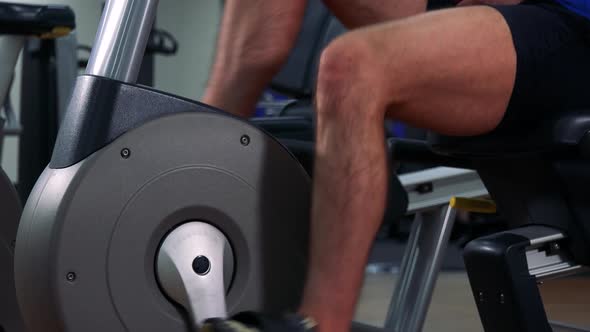 A Fit Man Trains on a Recumbent Bike in a Gym - Closeup on Legs