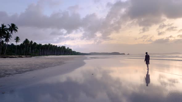 Young woman with short dress walking away from camera on wet sand creating reflections on endless As