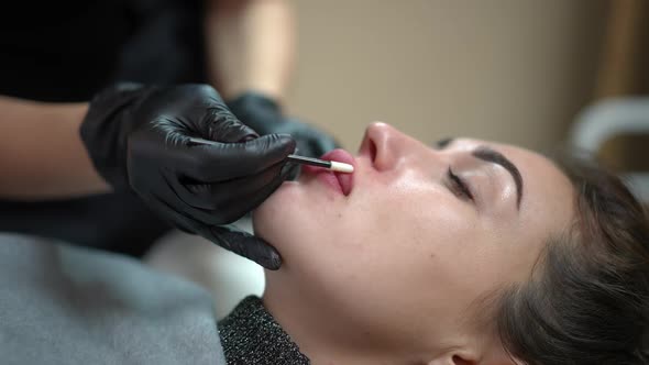 Beautician Tattoo Master Covering Tattooed Female Lips with Cream in Beauty Salon