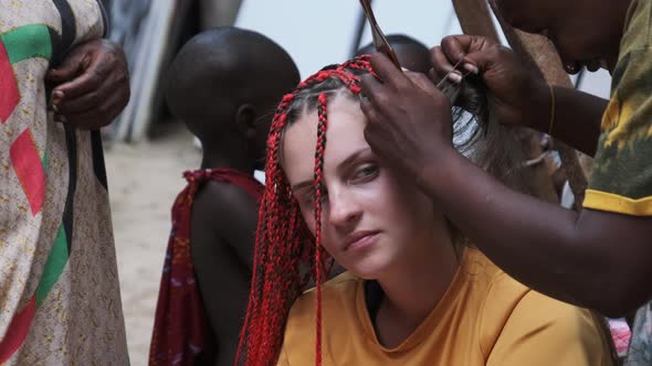 African Woman Weaving African Braids with Red Kanekalon Outdoor Zanzibar Africa