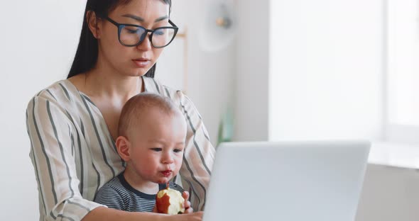 Young Mother Freelancer with Her Child Working at Home Office Using Laptop