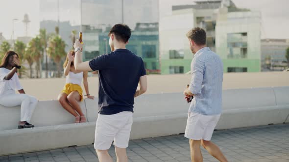 Group of Multiracial Young Happy Friends Drink Alcohol and Relax on Embankment on Summer Evening