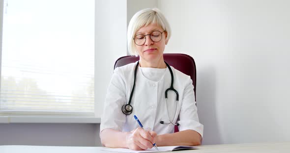 Mature woman doctor in a white coat with an stentoscope writes a medical prescription.