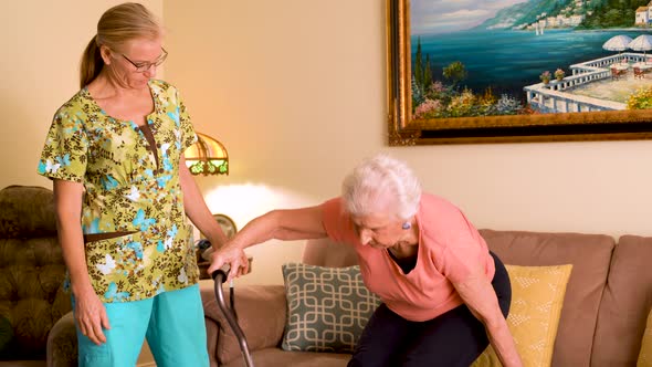 Closeup of home healthcare nurse helps elderly woman get up from couch and use a cane.