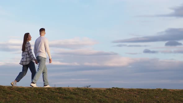 Walking Young Couple on the Background of a Beautiful Sky