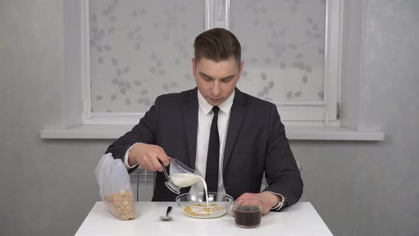 A Cheerful Young Man in a Suit Eats Cereal and Drinks Coffee