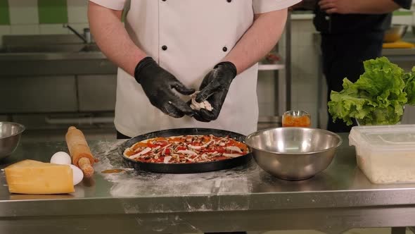 Closeup of the Chef Putting Mushrooms on Pizza with Tomatoes in the Kitchen