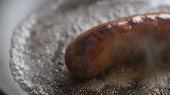 Camera follows cooking sausage on frying pan. Slow Motion.