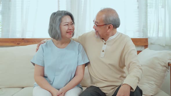 Portrait of Happy Asian Senior couple sit on sofa enjoy retirement life together  at house.