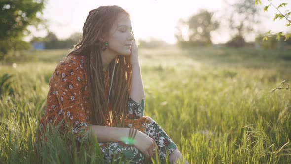 Beautiful Hippie Woman with Dreadlocks in Green Grass at Sunset Having Good Time Outdoors