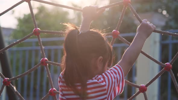 Cute little girl climbing on rope mesh at playground. Happy little girl having fun in the playground