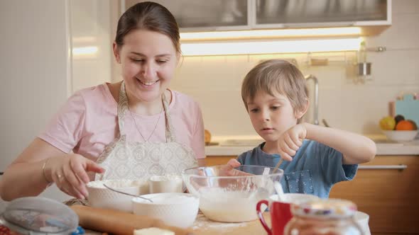 Happy Mother with Little Son Stirring and Mixing Dough Ingredients in Big Glass Bowl