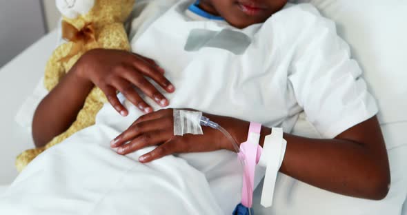 Sick girl resting with teddy bear on bed