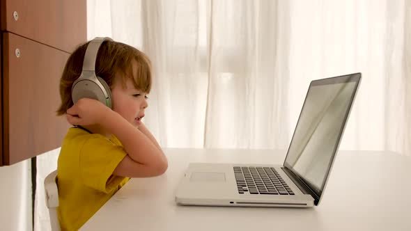 Child Listens To Music on Headphones in Front of Laptop