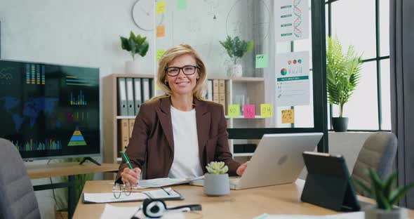 business woman with glasses using tablet computer and working documents sitting at workplace