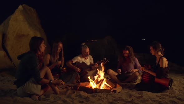 Friends Speaking Smiling Playing on Instruments Sitting Near Bonfire at Night Beach