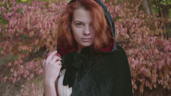 Mysterious Red-haired Caucasian Girl in a Black Gown Turning To the Camera and Proposing the Red