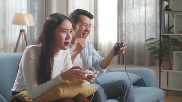 Asian Couple With Joystick Play Video Game On Tv, Male Celebrating Victory And Female Disappointed